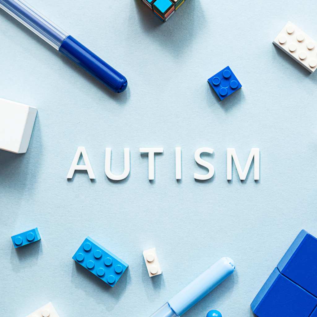 Blue toys and pens arranged around the word Autism on a light blue background